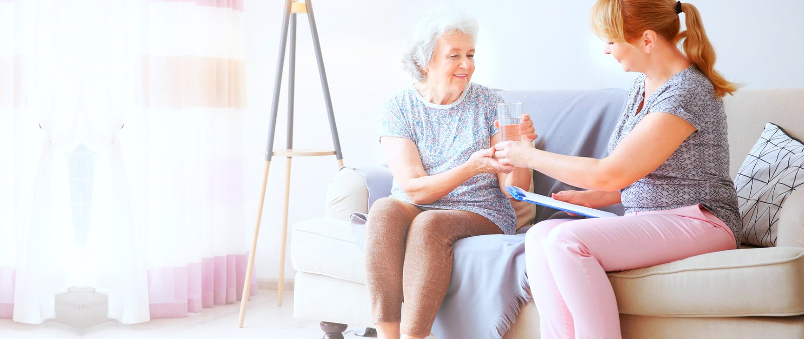 caretaker giving water to an elderly woman